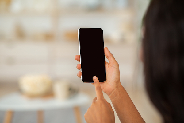 Working or studying from home remotely. African American woman touching mobile phone screen with mockup for mobile app or website design, indoors. Black lady using modern gadget